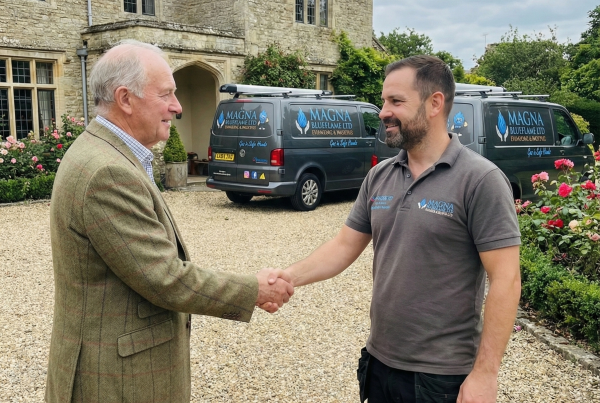 Two men shaking hands outside a home, with a Magna BlueFlame service van in the background, symbolizing trust and professionalism in plumbing and heating services.