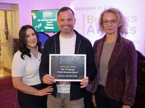 Three people stand indoors, smiling at the camera. The man in the centre holds a framed award for the TC Group Family Business Award 2026. A purple business awards sign is visible in the background, as they proudly commemorate Celebrating 15 Years: How Magna Blueflame Became Dorset’s Trusted Heating Experts.
